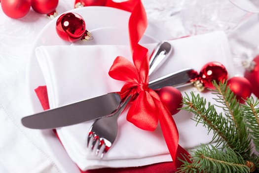 Romantic Christmas table with red balls and red bow with cutlery knife and fork on a napkin