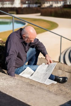 Middle-aged man,senior sitting with a newspaper on a staircase in spring outdoors