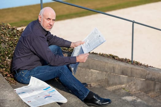 Middle-aged man,senior sitting with a newspaper on a staircase in spring outdoors