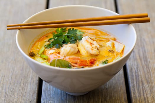 Bowl plate with freshly prepared Tom Yam soup with clanguste and coriander with chopsticks as close-up