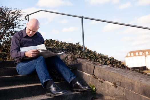 Middle-aged man,senior sitting with a newspaper on a staircase in spring outdoors