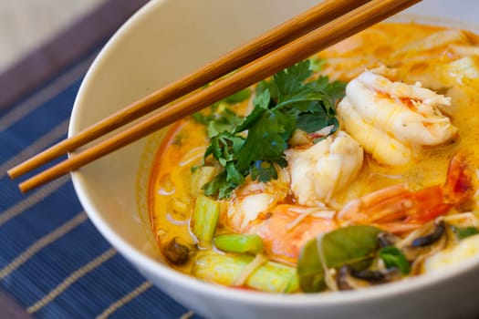 Bowl plate with freshly prepared Tom Yam soup with clanguste and coriander with chopsticks as close-up