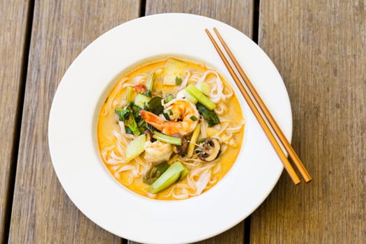 Bowl plate with freshly prepared Tom Yam soup with clanguste and coriander with chopsticks as close-up