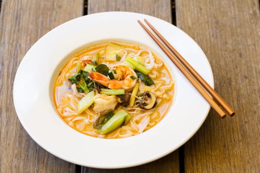 Bowl plate with freshly prepared Tom Yam soup with clanguste and coriander with chopsticks as close-up