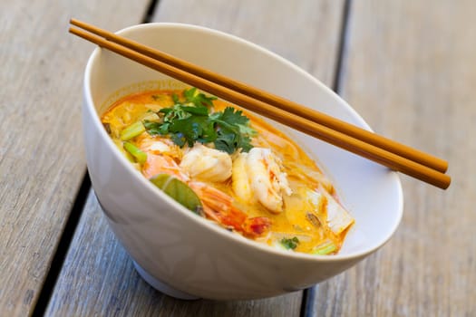 Bowl plate with freshly prepared Tom Yam soup with clanguste and coriander with chopsticks as close-up
