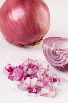 Red food onion whole and in small cubes Brunoise in a bowl on a white wooden board