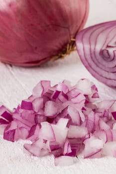 Red food onion whole and in small cubes Brunoise in a bowl on a white wooden board