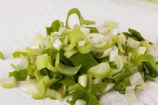 Leek spring onions with root as a whole and cut as a close-up on a white wooden board