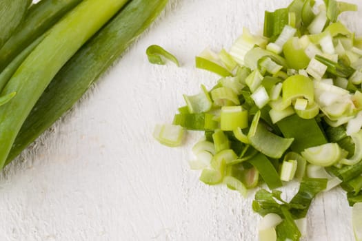 Leek spring onions with root as a whole and cut as a close-up on a white wooden board