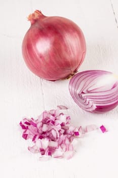 Red food onion whole and in small cubes Brunoise in a bowl on a white wooden board