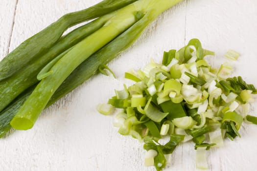 Leek spring onions with root as a whole and cut as a close-up on a white wooden board