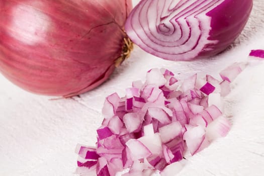 Red food onion whole and in small cubes Brunoise in a bowl on a white wooden board