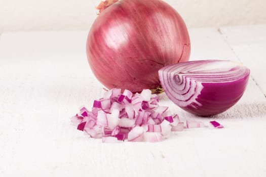 Red food onion whole and in small cubes Brunoise in a bowl on a white wooden board