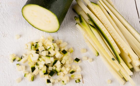Fresh zucchini all in julienne strips and cut into brunoise cubes on a white hoözboard