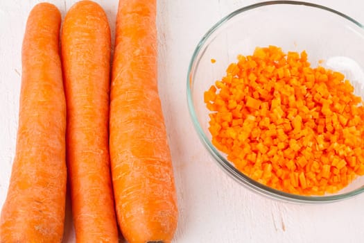 Fresh carrots beet root beet as whole and finely diced brunoise in a bowl on a white wooden board