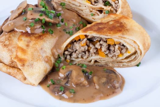 Pancake crepes tortillas stuffed with mushrooms and minced meat on a white plate close-up