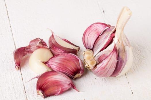 Garlic tuber with toes Fresh in whole and as a detail as a close-up on white wood