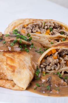 Pancake crepes tortillas stuffed with mushrooms and minced meat on a white plate close-up