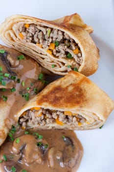 Pancake crepes tortillas stuffed with mushrooms and minced meat on a white plate close-up