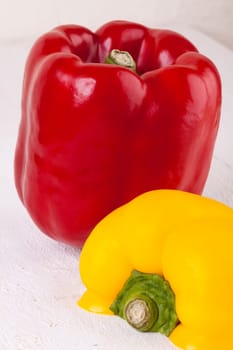 Fresh red and yellow peppers on a white wooden board as a close-up