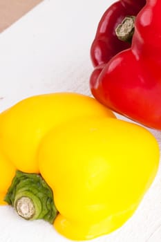 Fresh red and yellow peppers on a white wooden board as a close-up