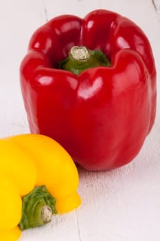 Fresh red and yellow peppers on a white wooden board as a close-up