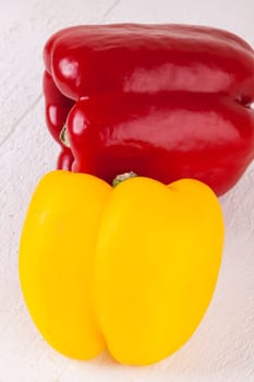 Fresh red and yellow peppers on a white wooden board as a close-up