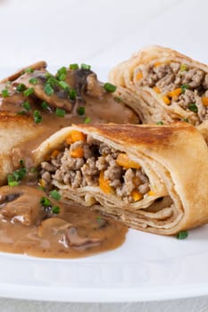 Pancake crepes tortillas stuffed with mushrooms and minced meat on a white plate close-up