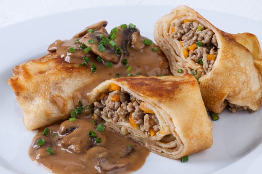 Pancake crepes tortillas stuffed with mushrooms and minced meat on a white plate close-up