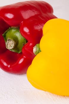 Fresh red and yellow peppers on a white wooden board as a close-up