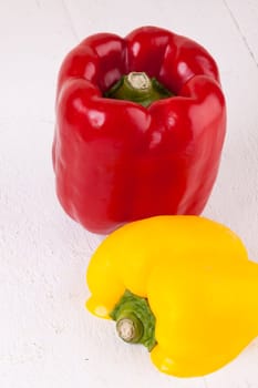 Fresh red and yellow peppers on a white wooden board as a close-up
