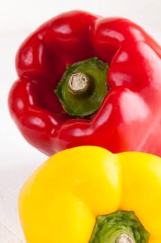 Fresh red and yellow peppers on a white wooden board as a close-up