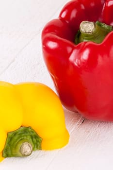 Fresh red and yellow peppers on a white wooden board as a close-up