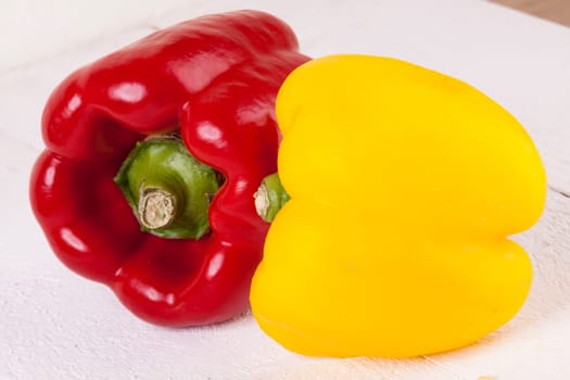 Fresh red and yellow peppers on a white wooden board as a close-up