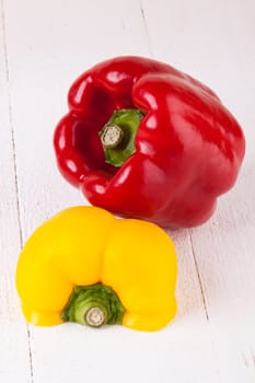 Fresh red and yellow peppers on a white wooden board as a close-up