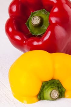 Fresh red and yellow peppers on a white wooden board as a close-up