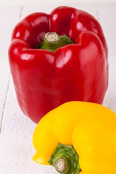 Fresh red and yellow peppers on a white wooden board as a close-up