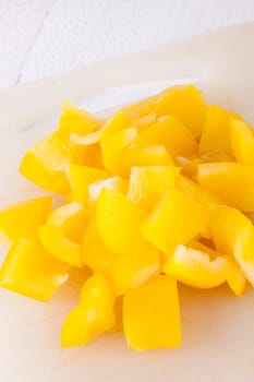 shaved yellow peppers in cubes on a rustic wooden board as a close-up