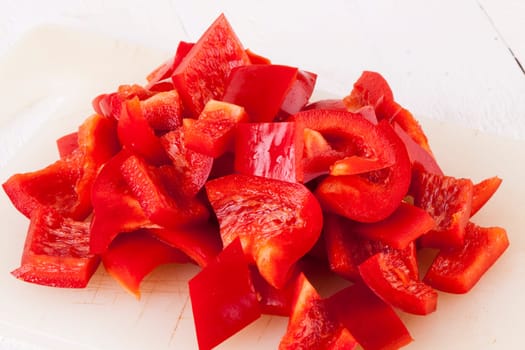 shaved red peppers in cubes on a rustic wooden board as a close-up