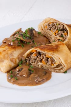 Pancake crepes tortillas stuffed with mushrooms and minced meat on a white plate close-up