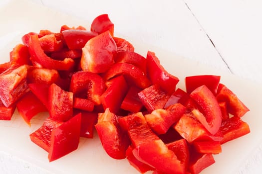 shaved red peppers in cubes on a rustic wooden board as a close-up
