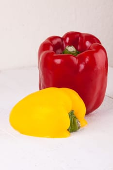 Fresh red and yellow peppers on a white wooden board as a close-up