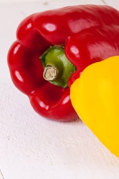 Fresh red and yellow peppers on a white wooden board as a close-up
