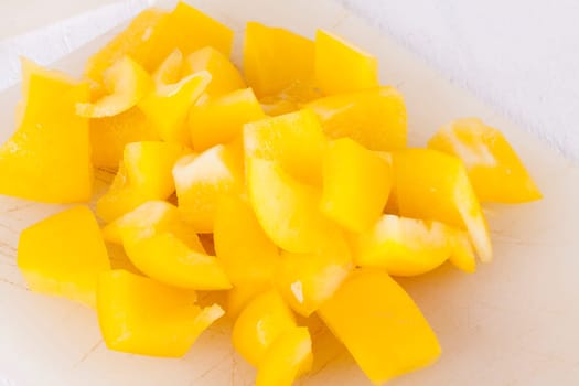 shaved yellow peppers in cubes on a rustic wooden board as a close-up
