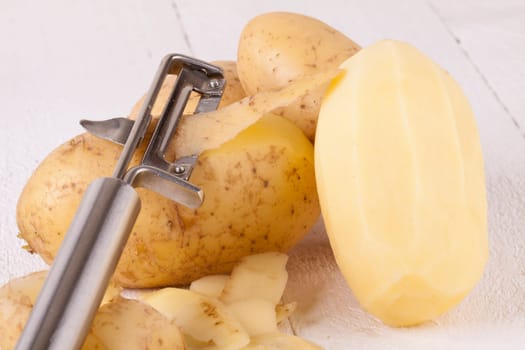 Potatoes with peels and peeled with potato peeler Peeler as close-up