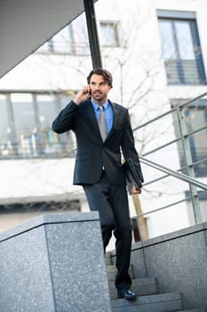 Young trendy successful businessman with mobile phone smartphone cheerful lyrane in front of an outdoor business building