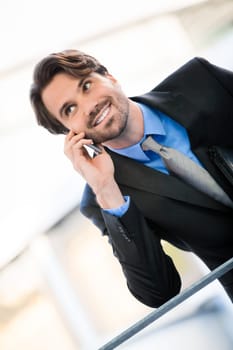 Young trendy successful businessman with mobile phone smartphone cheerful lyrane in front of an outdoor business building