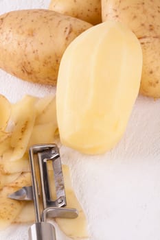 Potatoes with peels and peeled with potato peeler Peeler as close-up
