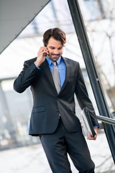 Young trendy successful businessman with mobile phone smartphone cheerful lyrane in front of an outdoor business building