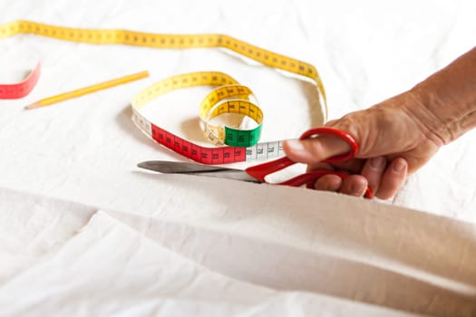 Hands with measuring tape scissors and pen when measuring fabric for the tailoring textile as a close-up